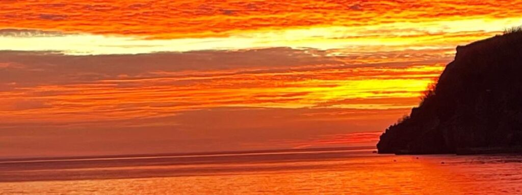 Spacious Orange sunrise in January with clouds and sea with dark brown headland